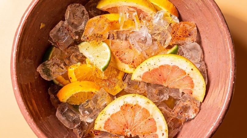 Close-up of a bowl filled with ice, orange slices, lime wedges, and grapefruit halves.