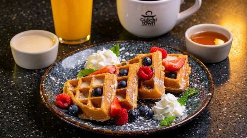 Golden waffles topped with berries, whipped cream, and powdered sugar, served with orange juice and coffee.