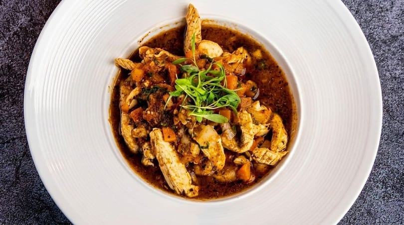 Chicken and vegetable stew in a rich brown sauce, garnished with fresh greens in a white bowl.