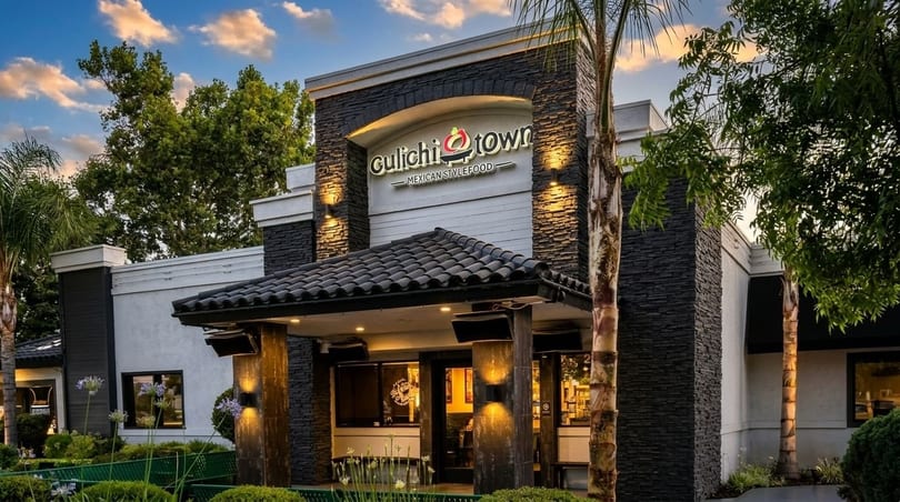 Exterior of Gulichi Town Mexican Style Food restaurant with stone facade, tiled roof entrance, and palm trees.