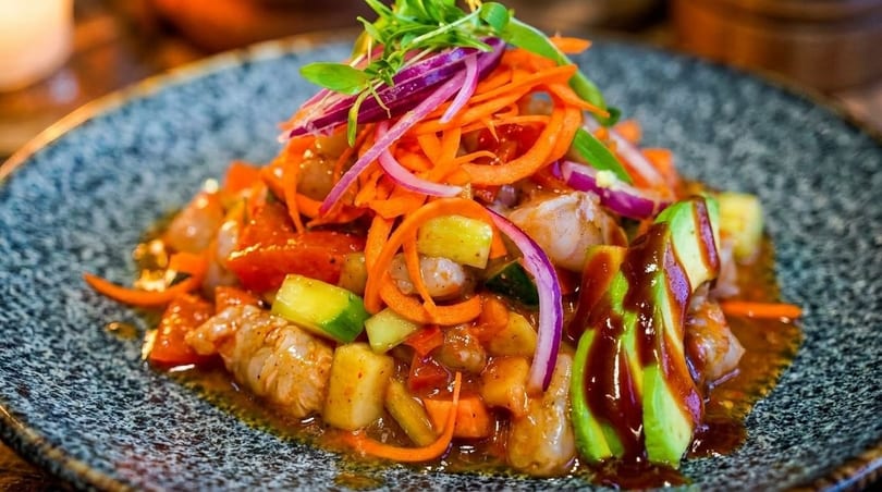 Shrimp ceviche with avocado, red onion, carrots, and cucumbers on a speckled gray plate.
