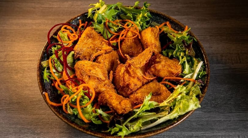 Crispy fried chicken pieces served on a bed of fresh green salad with shredded carrots and red beet.