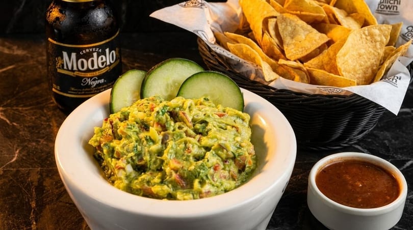 Guacamole with cucumber slices, a basket of tortilla chips, salsa, and a Modelo Negra beer.